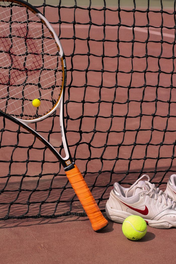 services-04 Tennis equipment including a racket, balls, and shoes on a clay court.