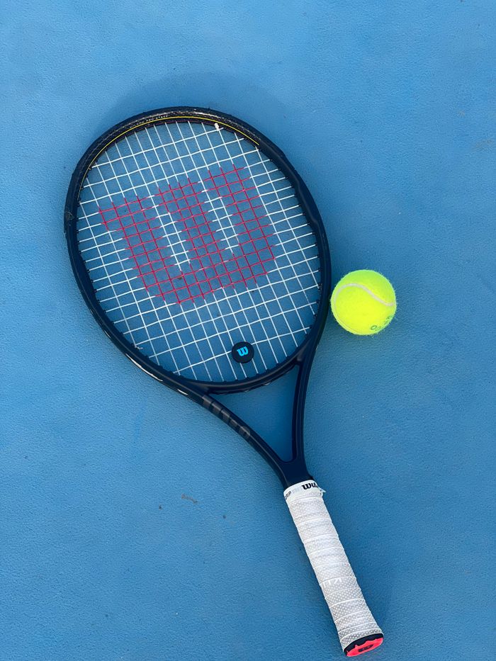 A tennis racket and bright yellow ball placed on a blue tennis court surface.