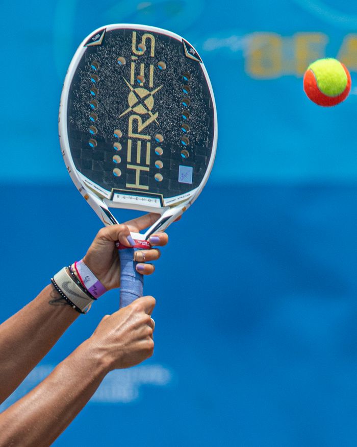 services-02 Close-up of a padel player hitting a neon ball with a racket, showcasing action sports.