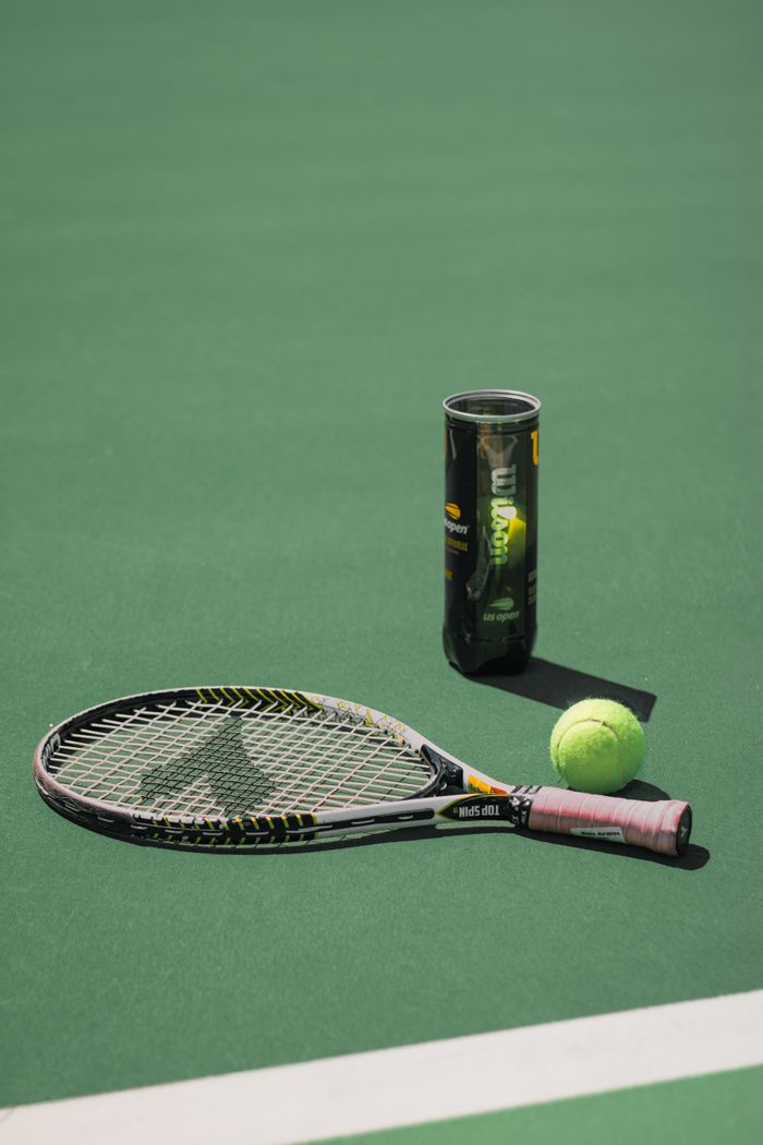 Tennis racket, balls, and can on a sunlit court, perfect for sports or leisure imagery.