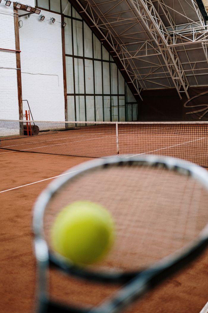 who-we-are Close-up view of a tennis racket and ball on an indoor clay court, showcasing the sport's dynamics.